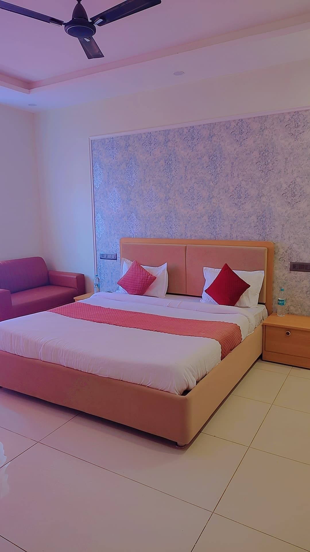 A bedroom with a bed, a nightstand, a red sofa, and a ceiling fan.