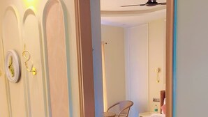 Une chambre d’hôtel avec un lit, un coin salon avec des coussins, une télévision et une salle de bain visible à travers une porte ouverte.
