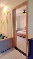 Habitación de hotel con cama, zona de estar con cojines, televisor y baño visible a través de una puerta abierta.