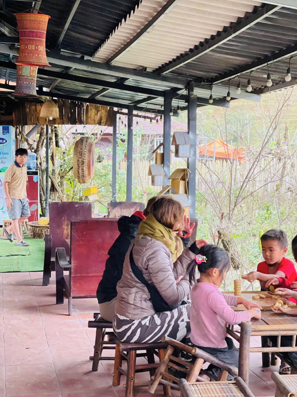 A covered outdoor seating area with wooden tables and chairs, a water dispenser, and hanging decorations.