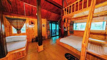 A cabin with wooden walls and floors, two bunk beds, a small table, and a window with a view.