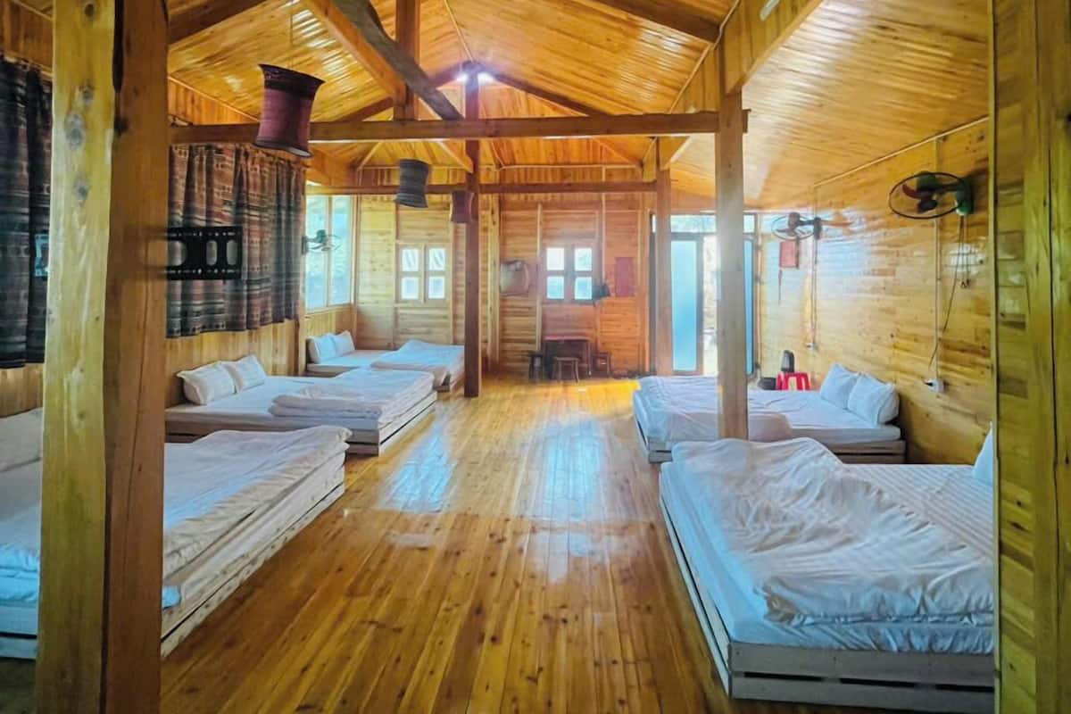 Una cabaña con cuatro camas de madera dispuestas en forma de U, una chimenea y un ventanal grande que deja entrar luz natural.