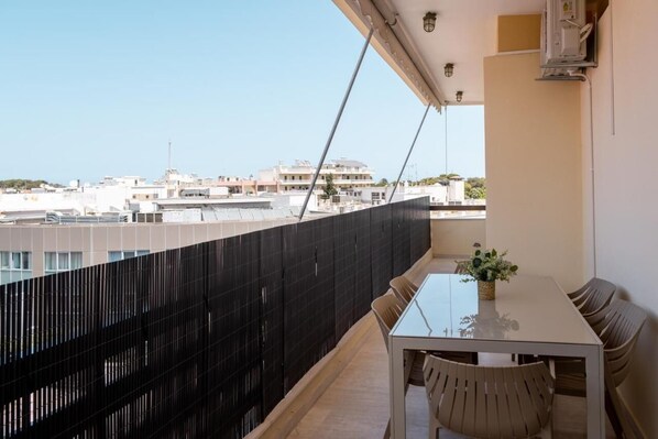 Uma varanda com mesa e cadeiras de vidro, com vista para um horizonte urbano com edifícios.