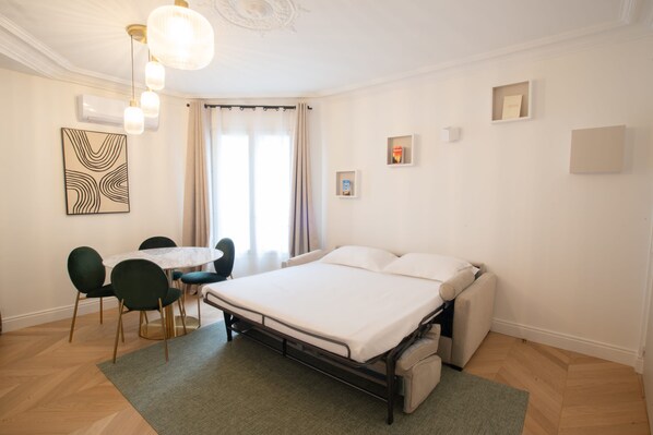 A modern hotel room with a large bed, a dining area with a table and chairs, and a chandelier.
