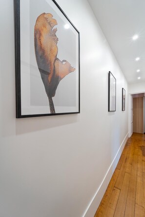 A hallway with framed artwork on the walls and wooden flooring.