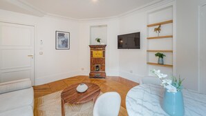 A modern living room with a wooden floor, a white sofa, a round table, a TV mounted on the wall, and a bookshelf with decorative items. - Madeleine Opéra - Excellent One Bedroom in Paris (Paris)