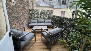 A balcony with a stone wall, a grey sofa, and a wooden table. - Madeleine Opéra - Excellent One Bedroom in Paris (Paris)