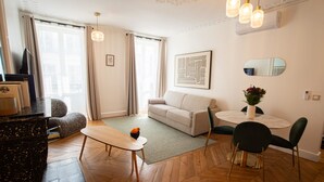 A modern living room with a sofa, a dining table with chairs, a TV, and a decorative mirror.