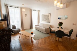 A modern living room with a sofa, a dining table with chairs, a TV, and a decorative mirror.