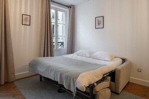 Une chambre à coucher avec un lit, des rideaux, une fenêtre et deux tableaux encadrés accrochés au mur.