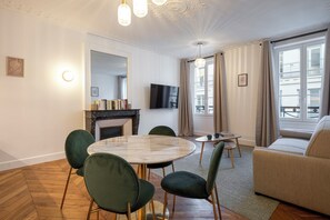 A modern living room with a fireplace, a round dining table with chairs, a sofa, and a TV mounted on the wall. - Madeleine Opéra - Excellent One Bedroom in Paris (Paris)