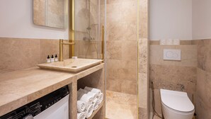 A modern bathroom with a glass-enclosed shower, a sink with toiletries, and a toilet.