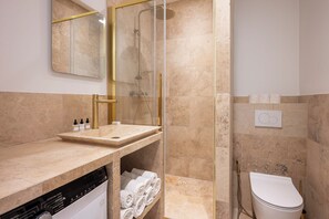 A modern bathroom with a glass-enclosed shower, a sink with toiletries, and a toilet.