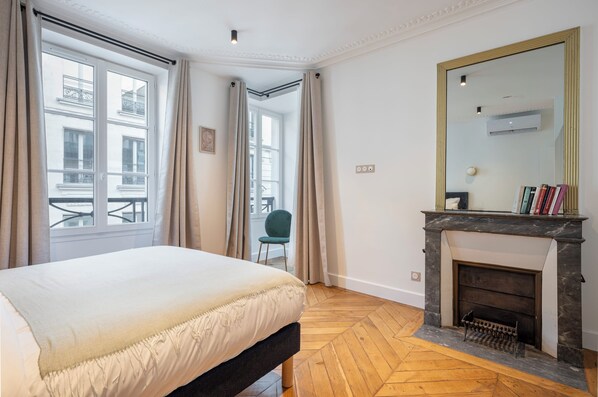 Une chambre à coucher avec un lit, une cheminée, un grand miroir et une vue sur l’extérieur.