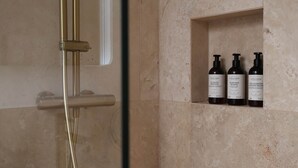 A bathroom with a shower, a glass door, and a shelf with three bottles of shampoo.