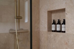 A bathroom with a shower, a glass door, and a shelf with three bottles of shampoo.