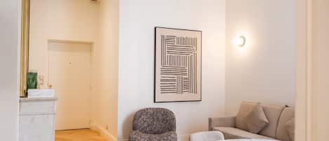 A modern living room with a sofa, a small armchair, a marble coffee table, and a framed abstract artwork on the wall.