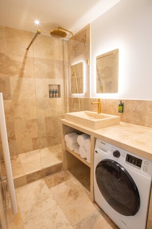A modern bathroom with a walk-in shower, a sink with a gold faucet, a mirror, and a built-in washing machine. - Madeleine Opéra - Excellent One Bedroom in Paris (Paris)