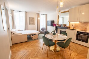 A modern hotel room with a convertible sofa bed, a dining area with a round table, and a kitchen with a built-in oven. - Madeleine Opéra - Excellent One Bedroom in Paris (Paris)