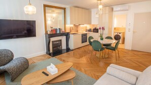 Een moderne woonkamer met een open haard, een eetgedeelte met groene stoelen en een keuken met houten kasten.
