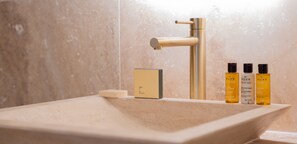 A bathroom with a beige sink, a gold faucet, and two NUXE shampoo bottles. - Madeleine Opéra - One Bedroom Deluxe in Paris (Paris)