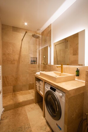 A modern bathroom with a built-in shower, a sink with a gold faucet, and a built-in washing machine.