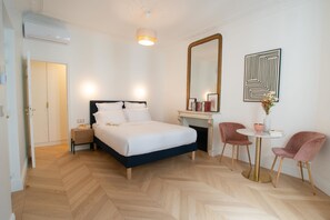 A hotel room with a bed, bedside table, a mirror, a desk with two chairs, and a small table with a vase.