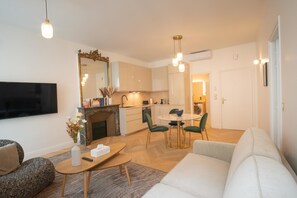 A modern living room with a flat-screen TV, a sofa, a coffee table, and a dining area with a table and chairs.