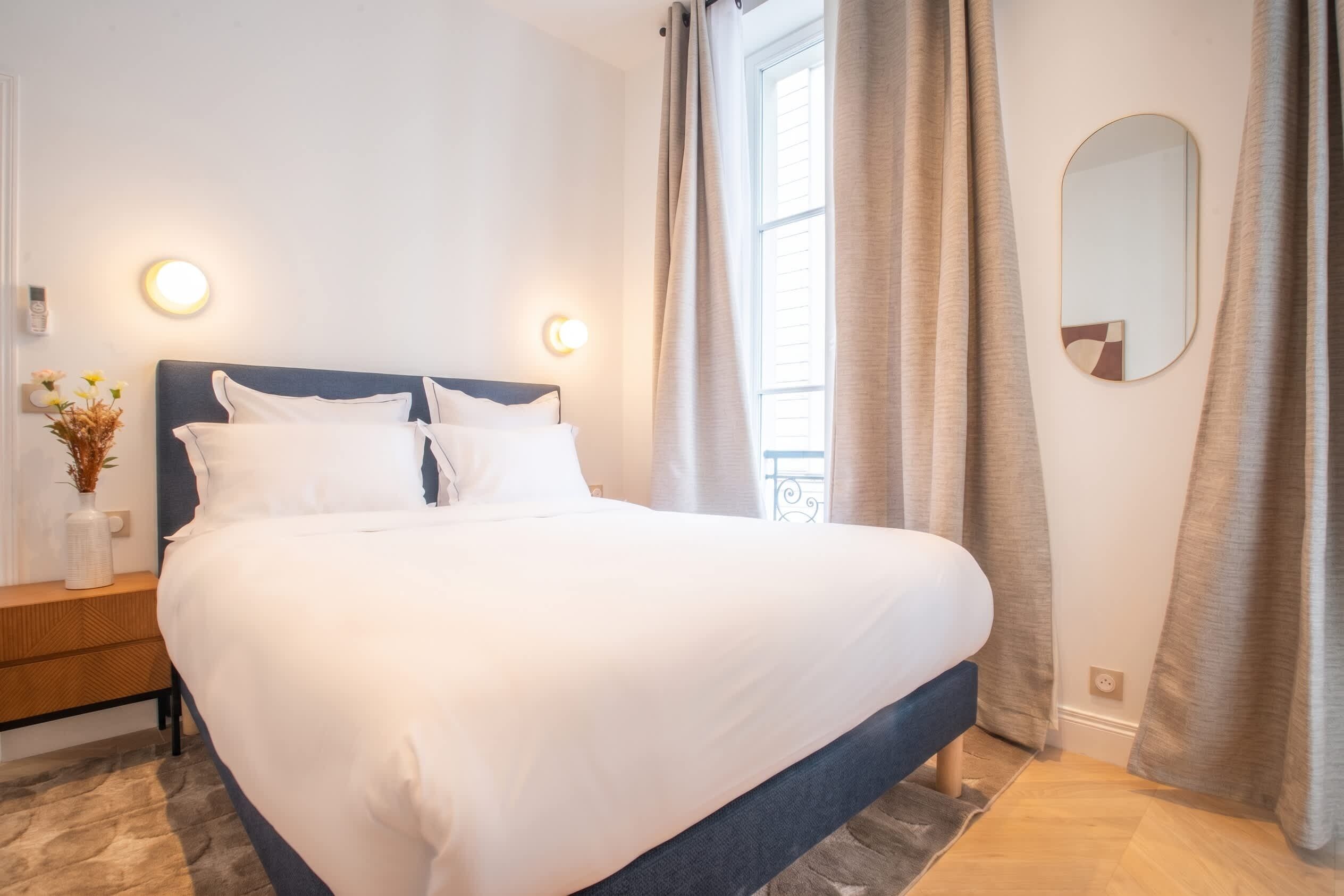 A neatly made bed in a hotel room with a headboard, bedside tables, and a mirror on the wall.