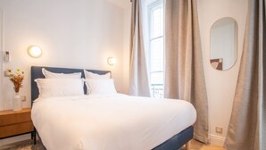 A neatly made bed in a hotel room with a headboard, bedside tables, and a mirror on the wall. - Madeleine Opéra - Excellent One Bedroom in Paris (Paris)