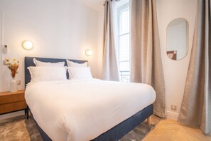 A neatly made bed in a hotel room with a headboard, bedside tables, and a mirror on the wall. - Madeleine Opéra - Excellent One Bedroom in Paris (Paris)