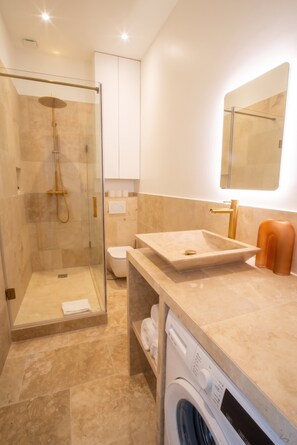 A modern bathroom with a glass-enclosed shower, a sink with a basin, and a washing machine. - Madeleine Opéra - Excellent One Bedroom in Paris (Paris)