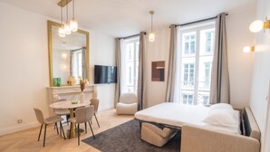 A modern hotel room with a bed, a desk with chairs, a television, and large windows. - Madeleine Opéra - Excellent One Bedroom in Paris (Paris)