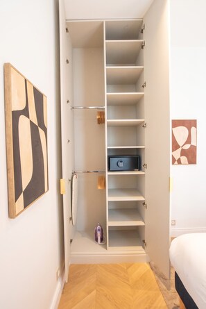 A walk-in closet with multiple shelves and hanging space, a small safe, and a bed in the adjacent room. - Madeleine Opéra - Excellent One Bedroom in Paris (Paris)