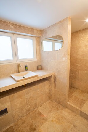 A bathroom with a beige tiled floor, a sink with a mirror above it, and a window above the sink.