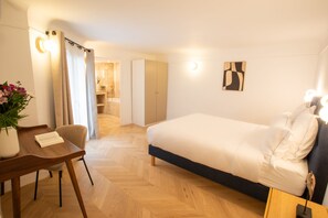 A hotel room with a bed, a desk, a chair, a potted plant, and a bathroom visible through an open door.