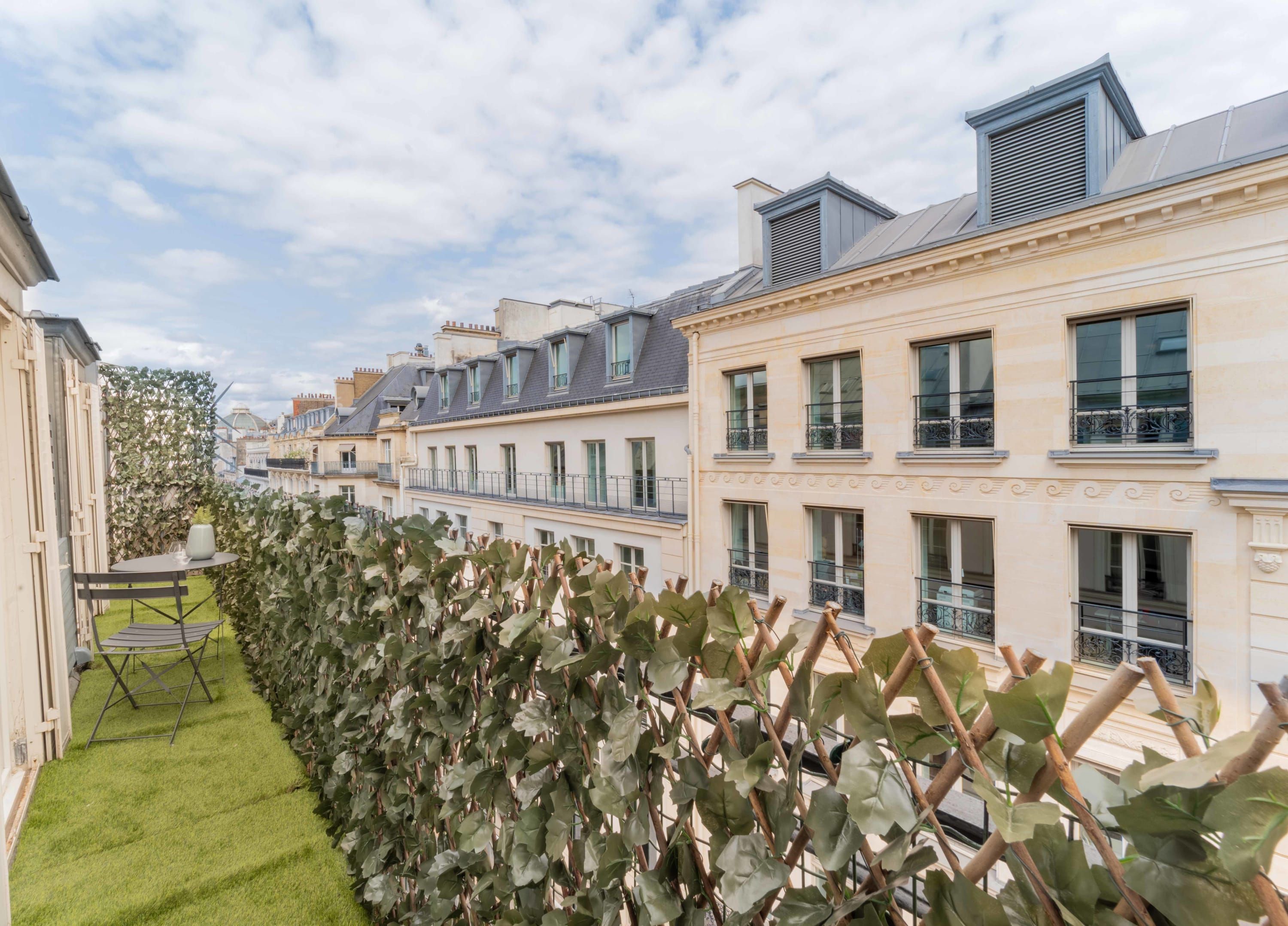 A row of townhouses with a green hedge and a small table with chairs on the left.