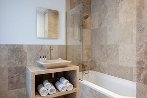 Un baño moderno con una bañera independiente, una ducha con mampara de vidrio y un revestimiento de mármol.