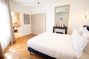 A hotel room with a large bed, a wardrobe, a mirror, and a small table with books. - Madeleine Opéra - Fabulous Two Bedroom in Paris (Paris)