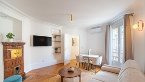 A modern living room with a flat-screen TV, a dining table with chairs, a sofa, and a decorative cabinet.