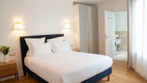 A neatly made bed with white linens, two wall-mounted lamps, and a wooden nightstand with a vase of flowers. - Madeleine Opéra - Excellent One Bedroom in Paris (Paris)