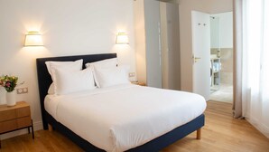 A neatly made bed with white linens, two wall-mounted lamps, and a wooden nightstand with a vase of flowers. - Madeleine Opéra - Excellent One Bedroom in Paris (Paris)
