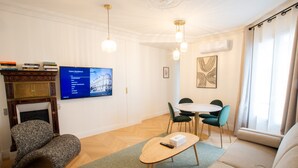 A living room with a fireplace, a television mounted on the wall, a dining area with a table and chairs, and a sofa. - Madeleine Opéra - Excellent One Bedroom in Paris (Paris)