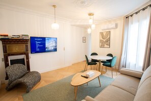A living room with a fireplace, a television mounted on the wall, a dining area with a table and chairs, and a sofa. - Madeleine Opéra - Excellent One Bedroom in Paris (Paris)