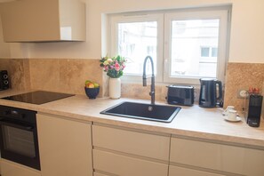 A modern kitchen with a built-in oven, a black sink, a coffee maker, and a window with a view of buildings. - Madeleine Opéra - One Bedroom Deluxe in Paris (Paris)