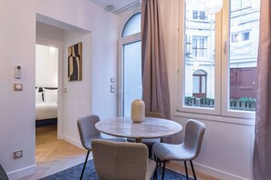 A modern hotel room with a round table, four chairs, a vase, a bed, and a view of the city through large windows. - Madeleine Opera - Very nice Apartment in Paris (Paris)