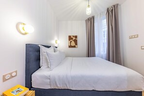 A neatly made bed with white linens, a blue headboard, and a bedside table with a book. - Madeleine Opera - Very nice Apartment in Paris (Paris)