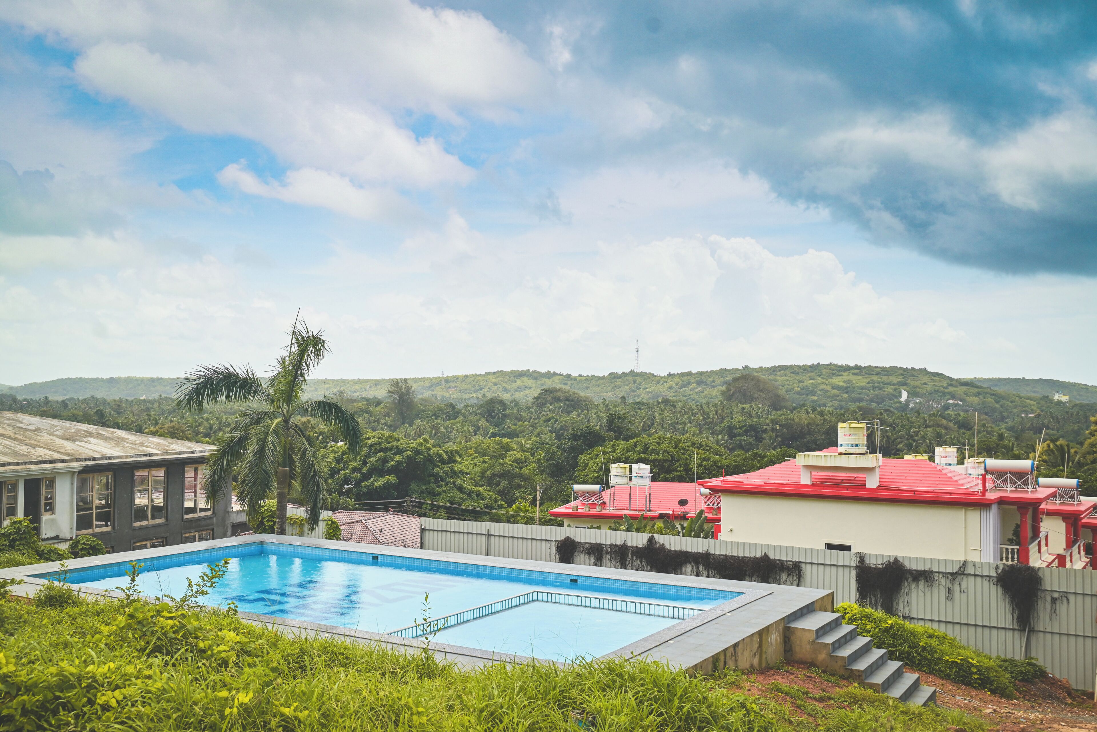 A swimming pool with a view of a red-roofed building and a hill in the background.