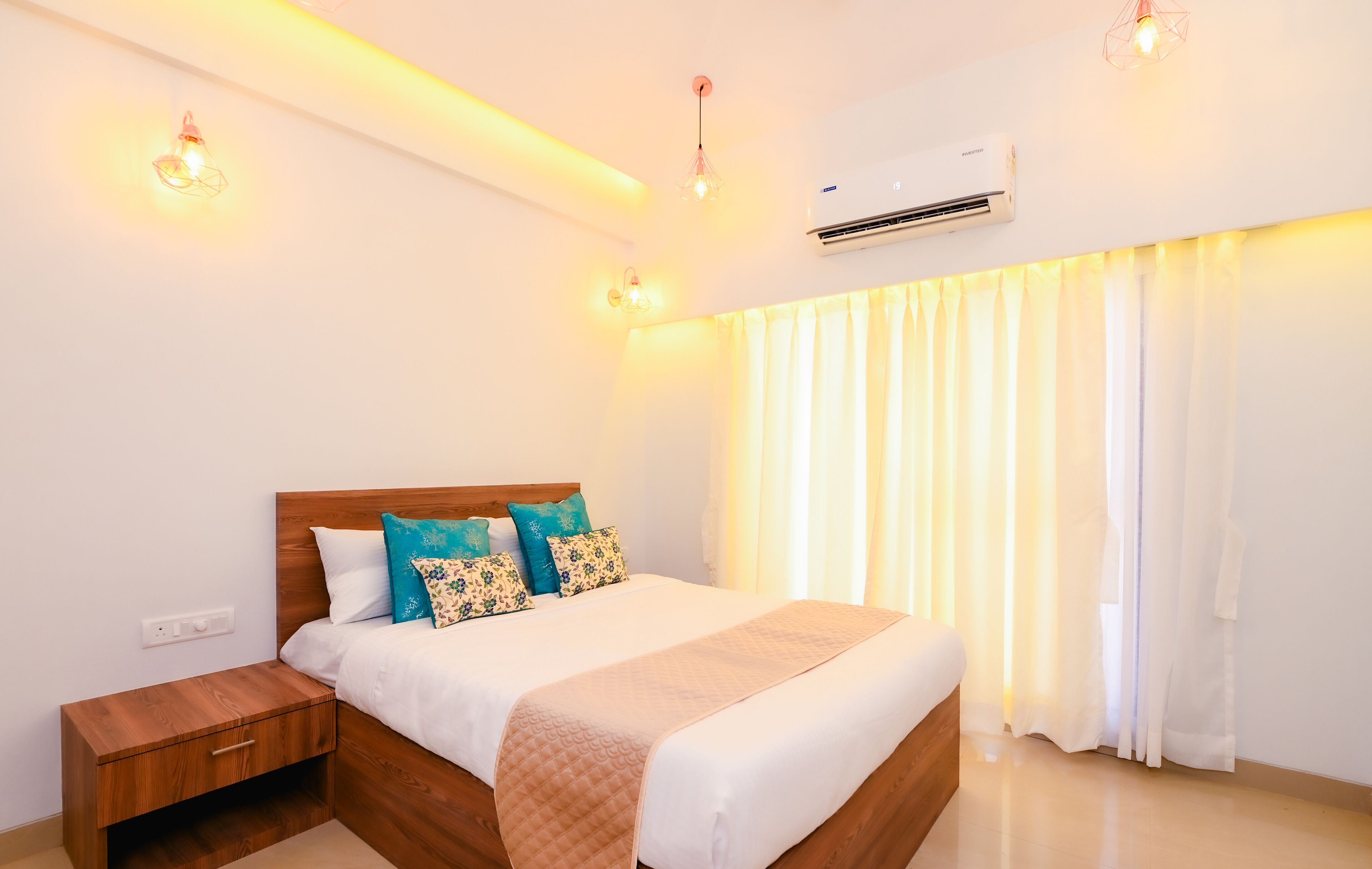 A modern bedroom with a wooden bed, white bedding, and decorative pillows. There is a nightstand with a drawer, a wall-mounted air conditioner, and a ceiling light fixture.