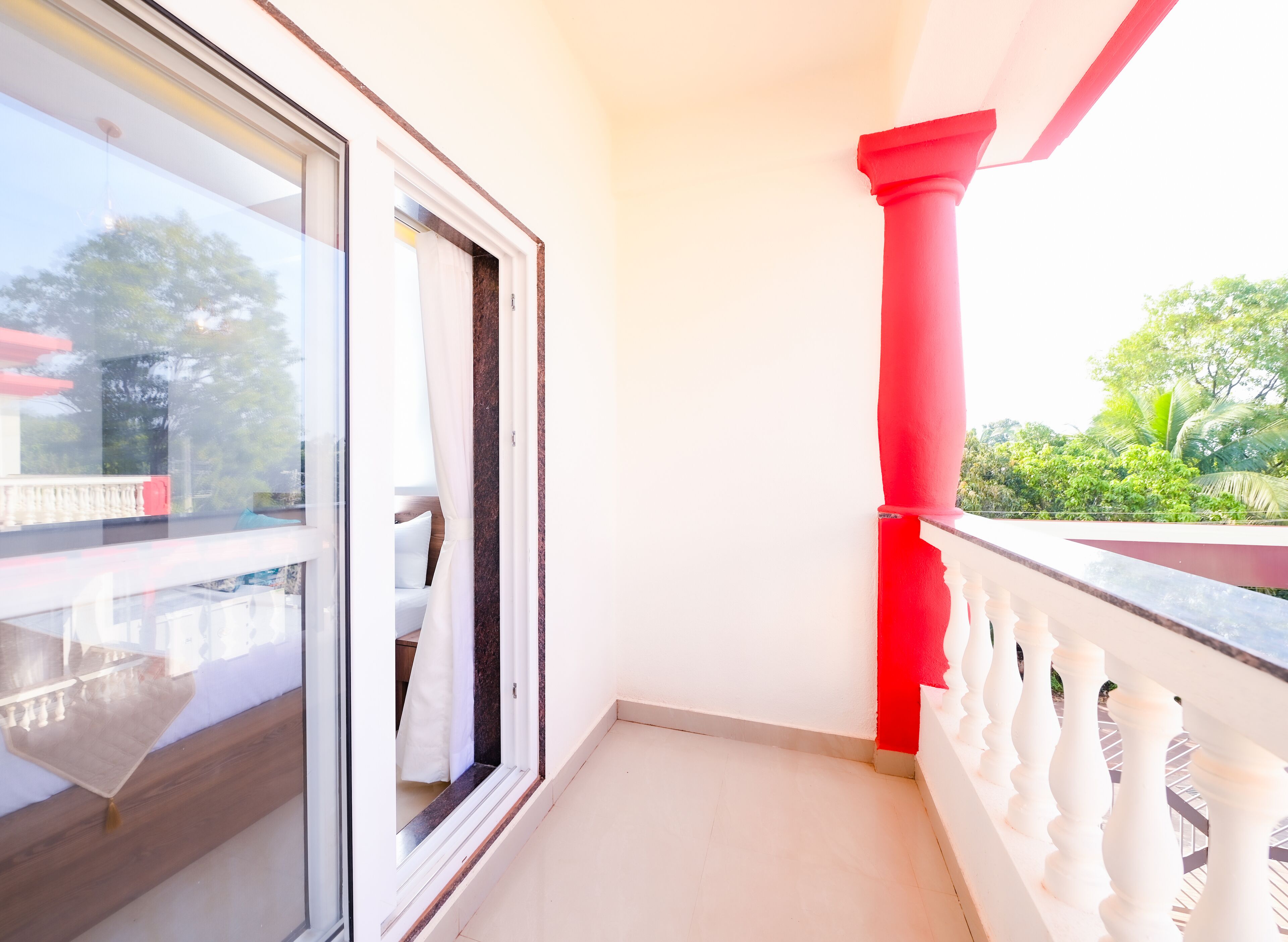 Uma varanda com porta de vidro que dá para um quarto, um pilar vermelho e um parapeito branco.